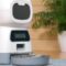 An unmarked white automatic pet food dispenser with a gray bowl sitting on the floor of a home.