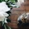 A tabby cat with mint green eyes staring up at the viewer while sitting on a wooden floor in front of large white flowers.